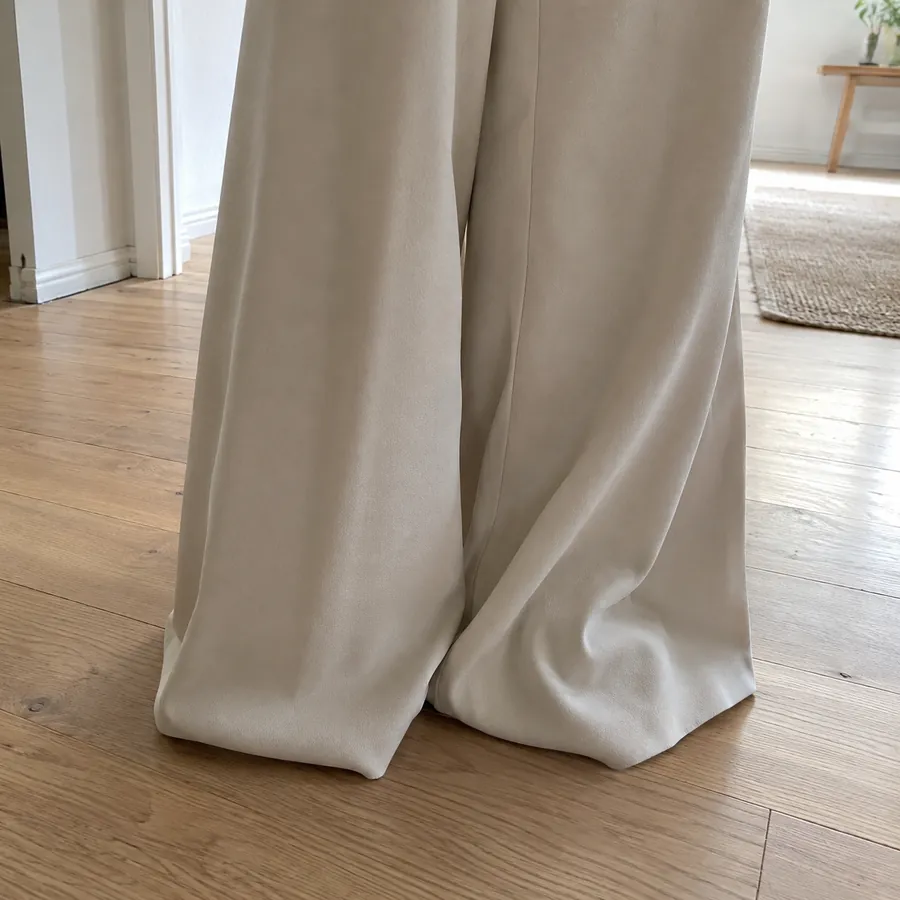 Close-up of wide crepe trouser legs falling straight to a wooden floor