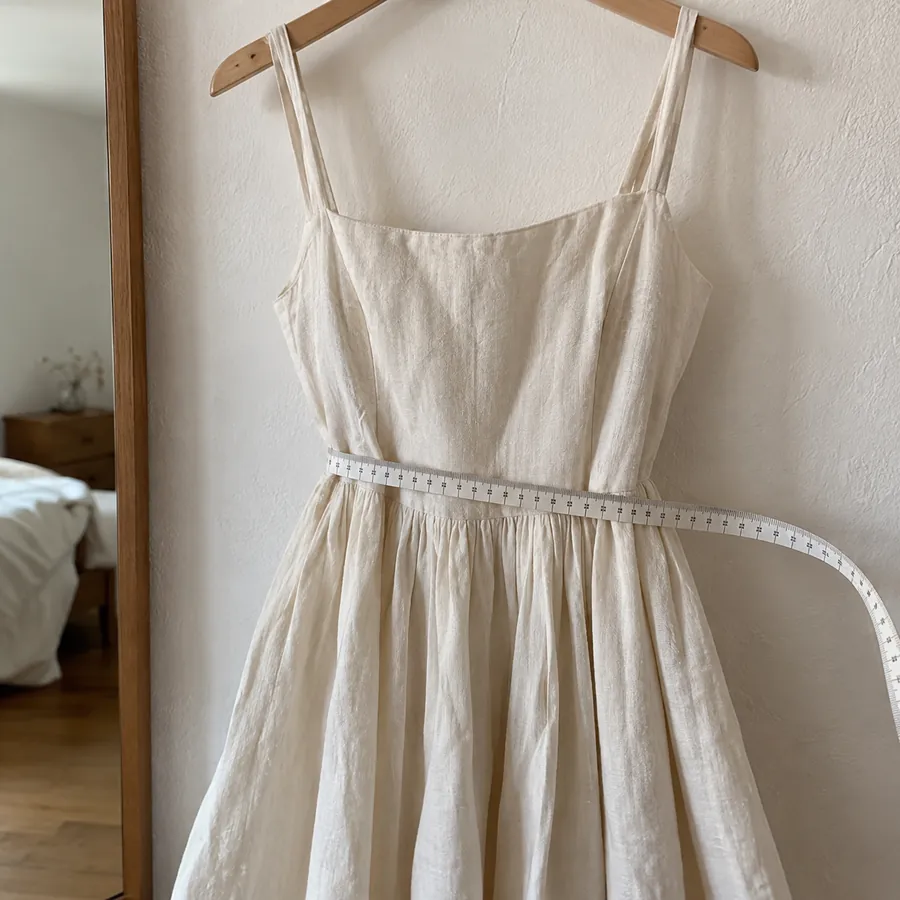 Soft measuring tape held at the waist of a cream linen dress hanging on a wall hook